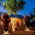 UrbanCamp Windhoek – illuminated African masks in the leafy camp garden