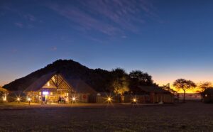 Sesriem desert camp – thatched bar building illuminated at dusk