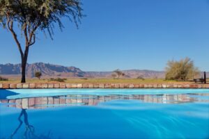 self-catering accommodation near Sossusvlei – pool and camel-thorn trees under blue sky